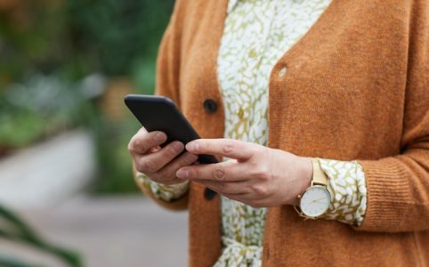 Kobieta w pomarańczowym sweterku trzyma w dłoni telefon