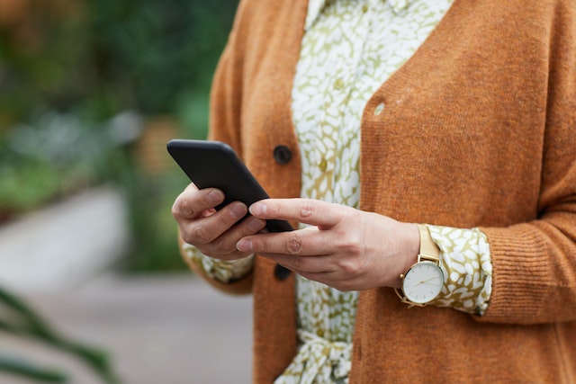Kobieta w pomarańczowym sweterku trzyma w dłoni telefon