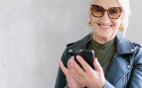 Starsza kobieta w okularach trzyma telefon w dłoni