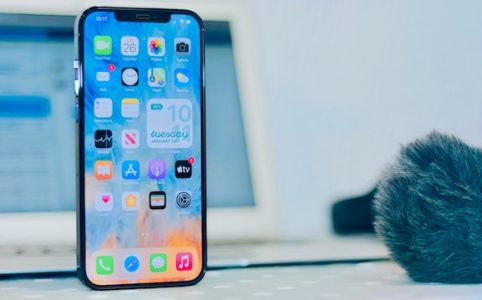 Telefon komórkowy z włączonym wyświetlaczem, w tle laptop