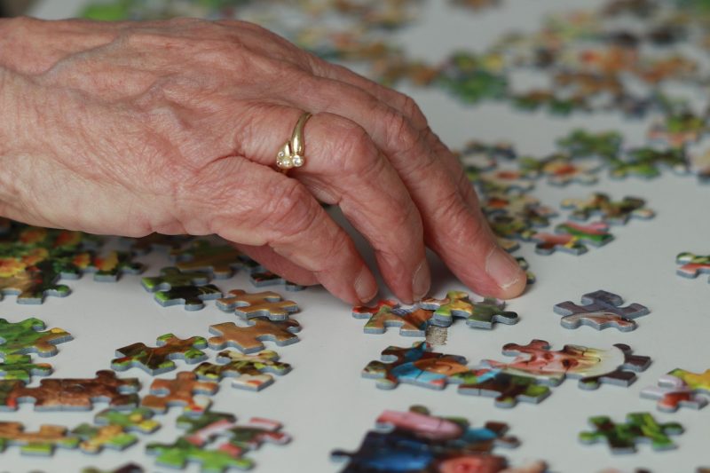 Dłoń starszej osoby układająca kolorowe puzzle na stole.